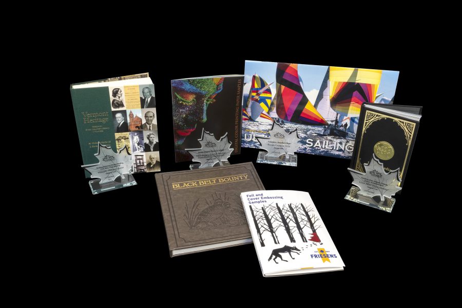 A collection of books arranged with Canadian Printing Awards–style maple leaf trophies displayed in front on a black background.