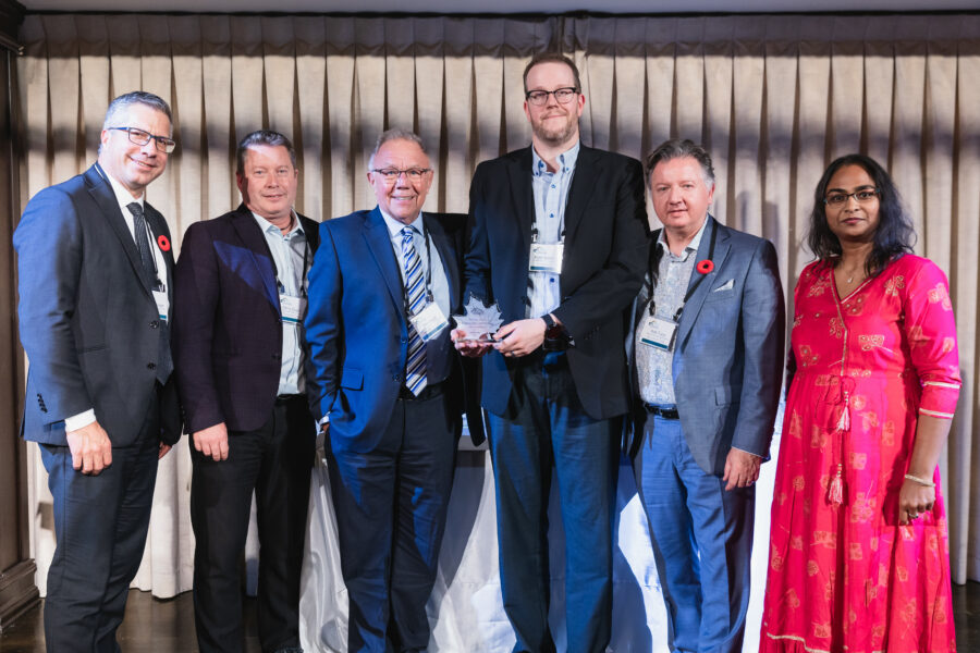 A group of six people standing together at an award ceremony, holding a maple‑leaf‑shaped Canadian Printing Awards trophy.