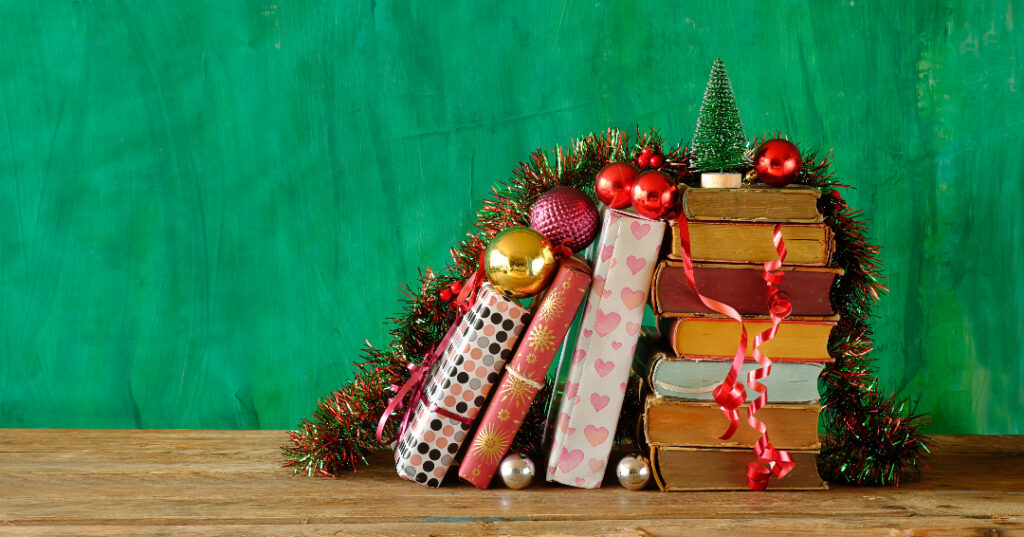 Wrapped books stacked with garland, ornaments, and a small tree against a green background.