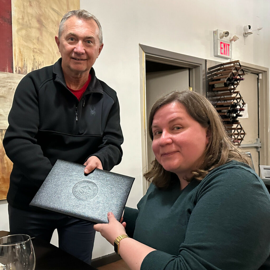 Two people holding an award folder during a recognition moment at an indoor event.