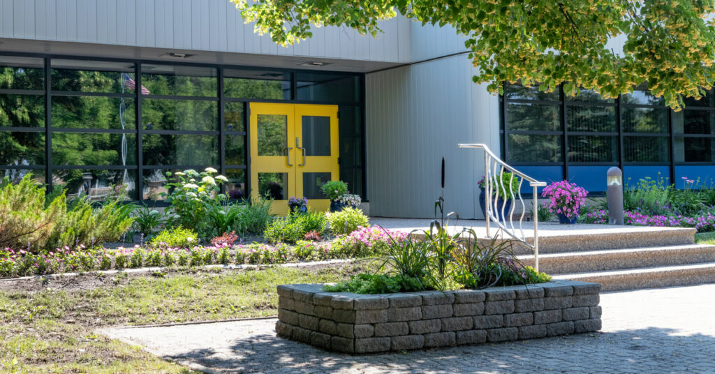 Exterior of the Friesens building with landscaped gardens, yellow doors, and a shaded walkway.