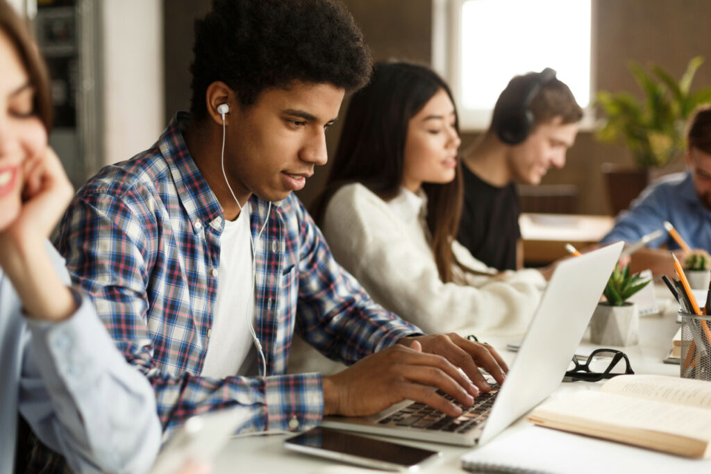 People working at a shared table with laptops, notebooks, and earbuds in a collaborative workspace.