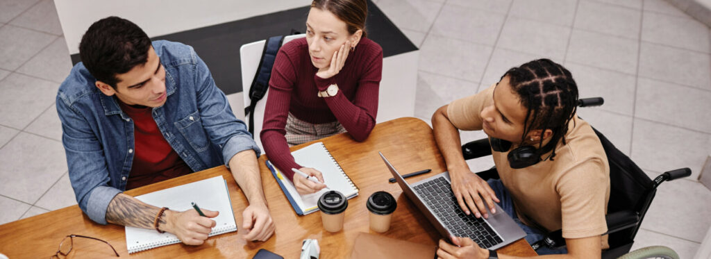 Group working together at a table with laptops, notebooks, and coffee during a collaborative meeting.