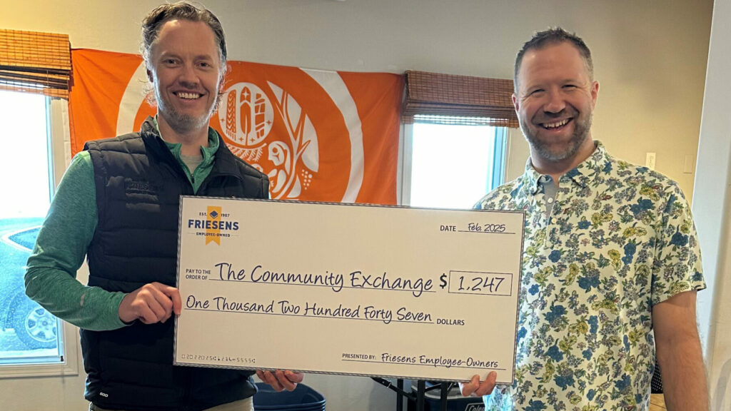 Two people holding a large donation cheque in a room with an orange banner in the background.