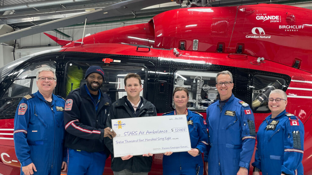 Group holding a large donation cheque in front of a red STARS Air Ambulance helicopter.