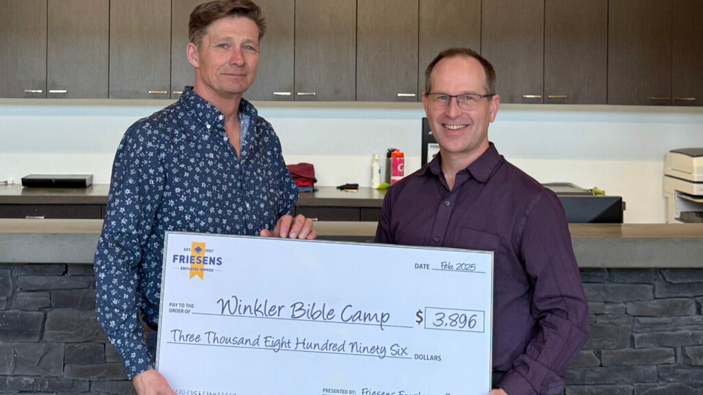 Two people holding a large donation cheque for Winkler Bible Camp inside a reception area.