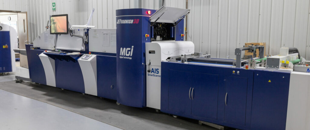 Blue MGI JETvarnish 3D spot UV coating machine in a production room.