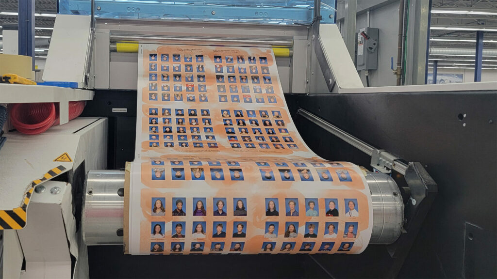 Printed photo sheets running through a press, showing rows of individual portraits on a continuous roll.