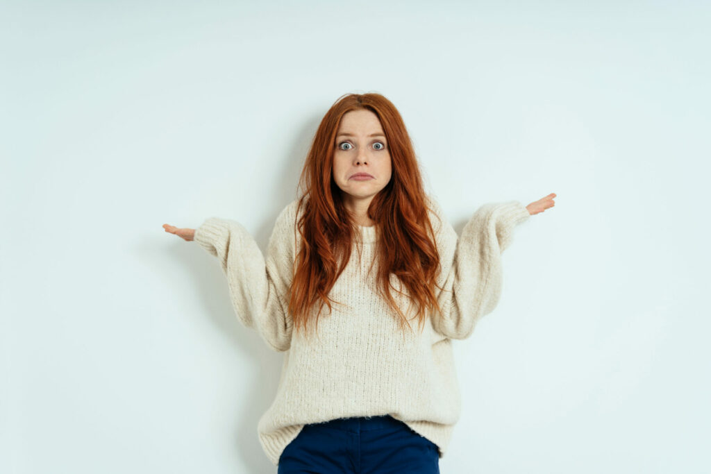 Person in a cozy sweater shrugging with both hands raised against a plain background.