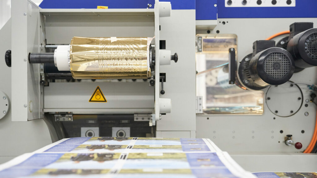 Foil stamping machine applying metallic foil to printed sheets on a production line