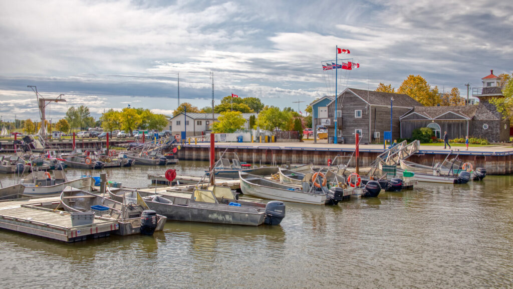 Small fishing boats docked at Gimli Harbour with buildings and Canadian flags in the background.