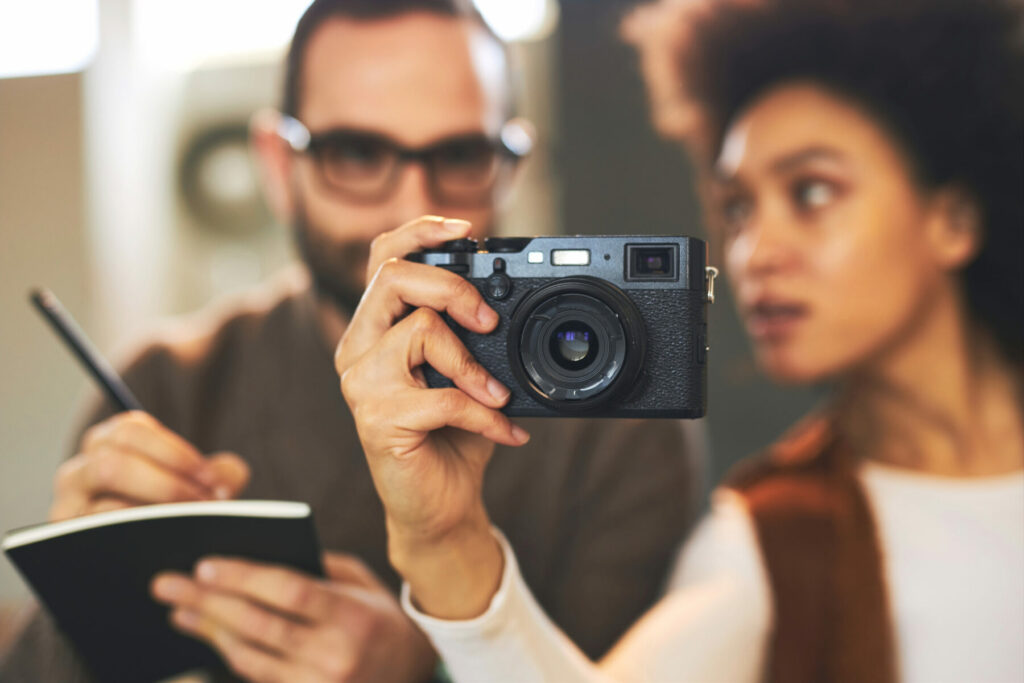 Person holding a camera while another takes notes during a hands‑on photography demonstration.