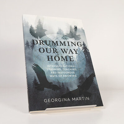 Book cover of Drumming Our Way Home featuring silhouetted birds over a blue forest background