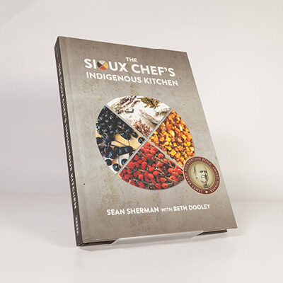 Book cover of The Sioux Chef’s Indigenous Kitchen featuring a circular food collage on a textured background