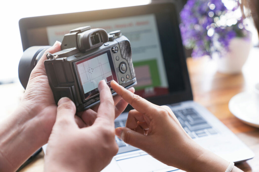 Hands pointing at a digital camera screen while reviewing an image in front of an open laptop.
