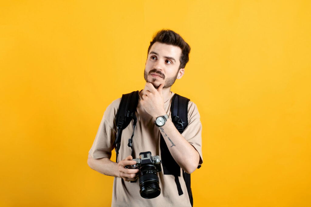 Person wearing a backpack and holding a camera against a bright yellow background.