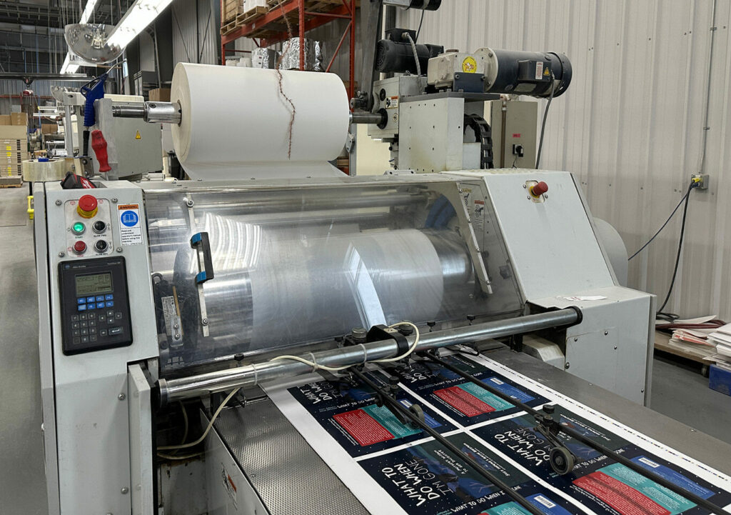 Close-up of a laminating machine applying clear film to printed book cover sheets in production.