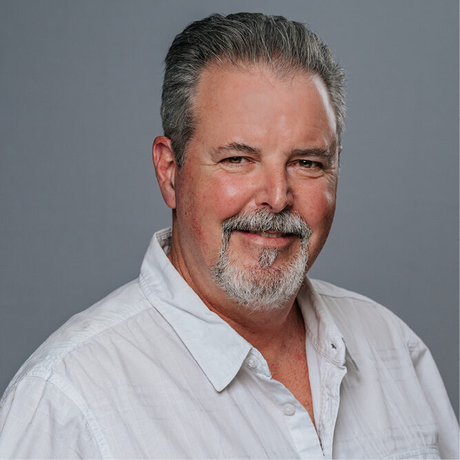 Person wearing a white button‑up shirt posed against a plain grey studio background