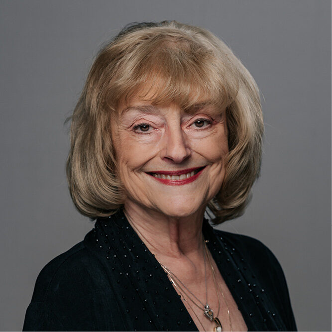 Person wearing a dark top and layered necklace against a neutral gray background.