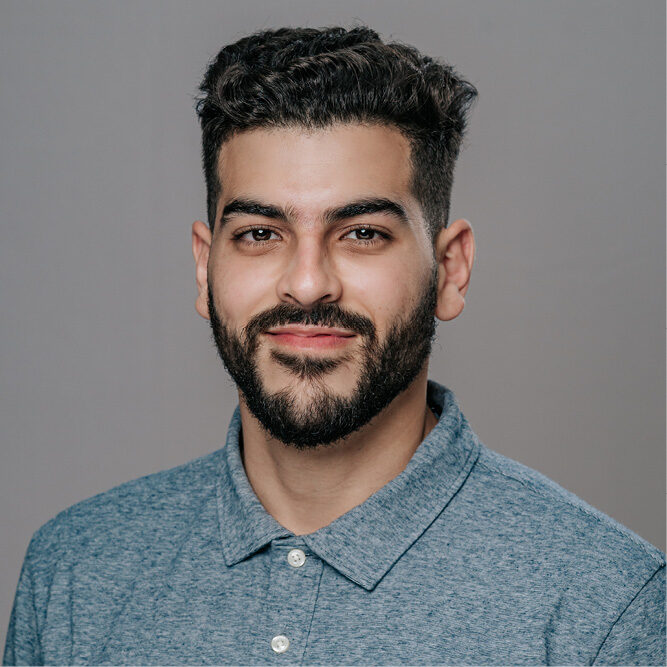 Person wearing a blue collared shirt posing against a plain grey background.