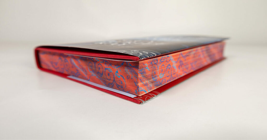 Close-up of a book with a bright red and blue sprayed edge featuring decorative patterns.