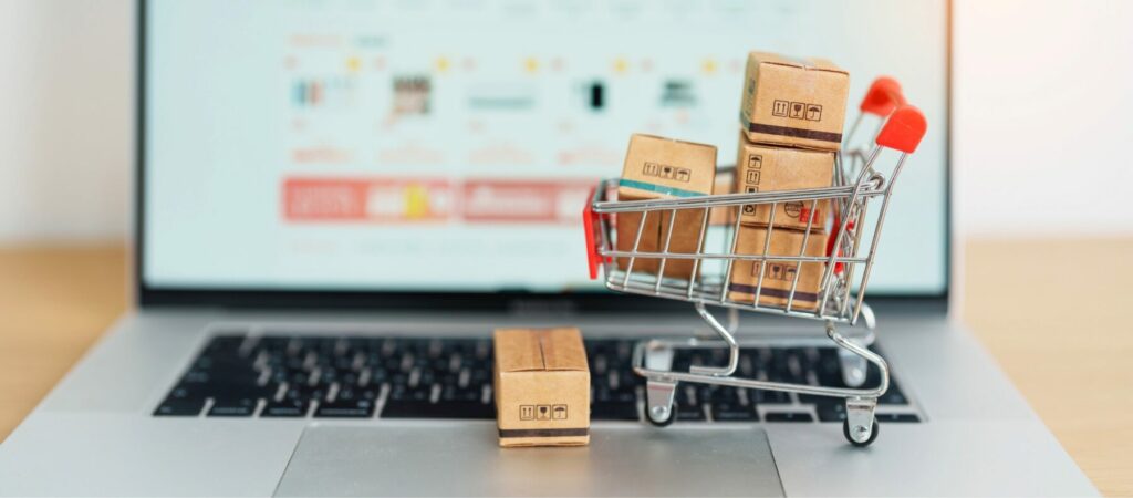 Small shopping cart filled with packages placed on a laptop displaying an online store.