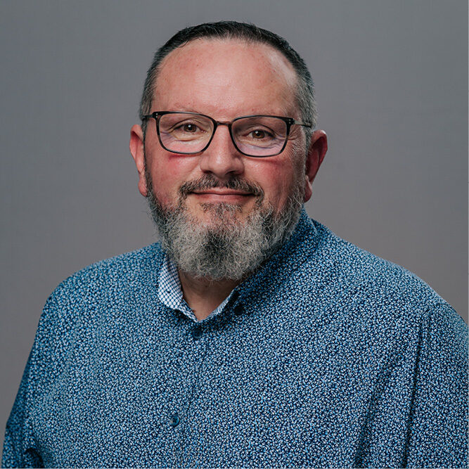 Person wearing a blue patterned shirt against a plain gray background.