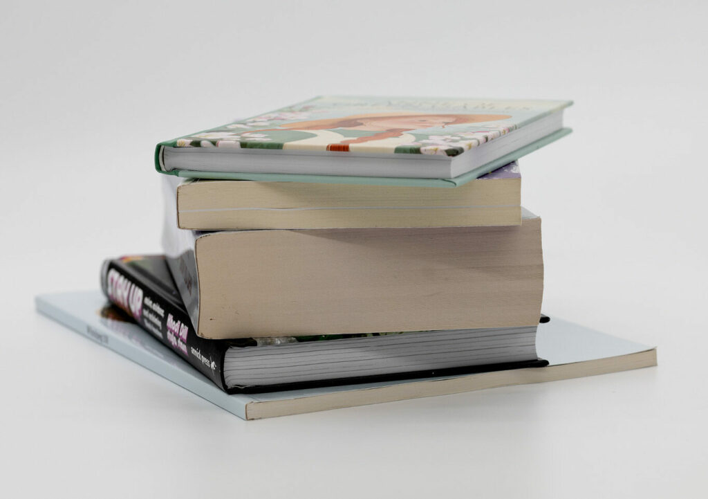 Stack of books with mixed bindings, including perfect bound and hardcover, arranged on a white background.