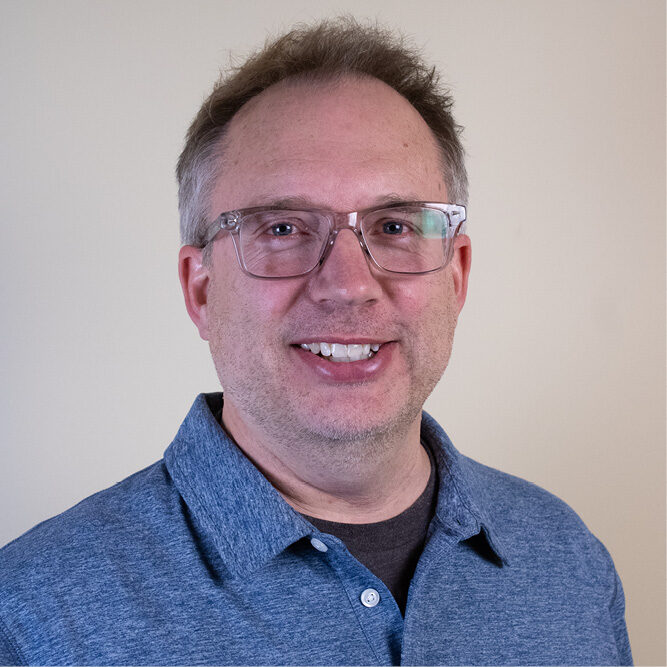 Person wearing a blue collared shirt posing for a professional headshot against a plain background.