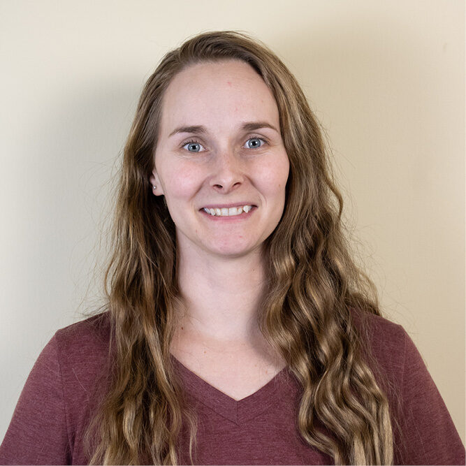 Person with long wavy hair wearing a maroon shirt against a plain background.