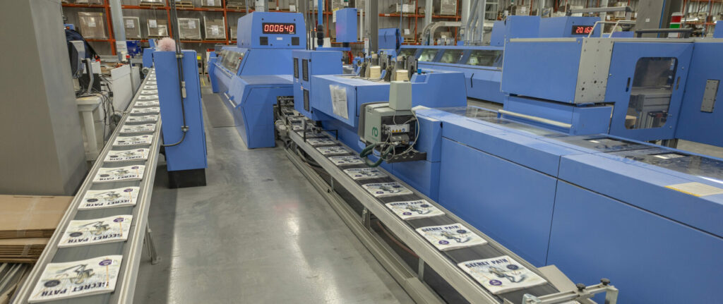 Perfect binding line with books moving along a conveyor in a large printing facility.