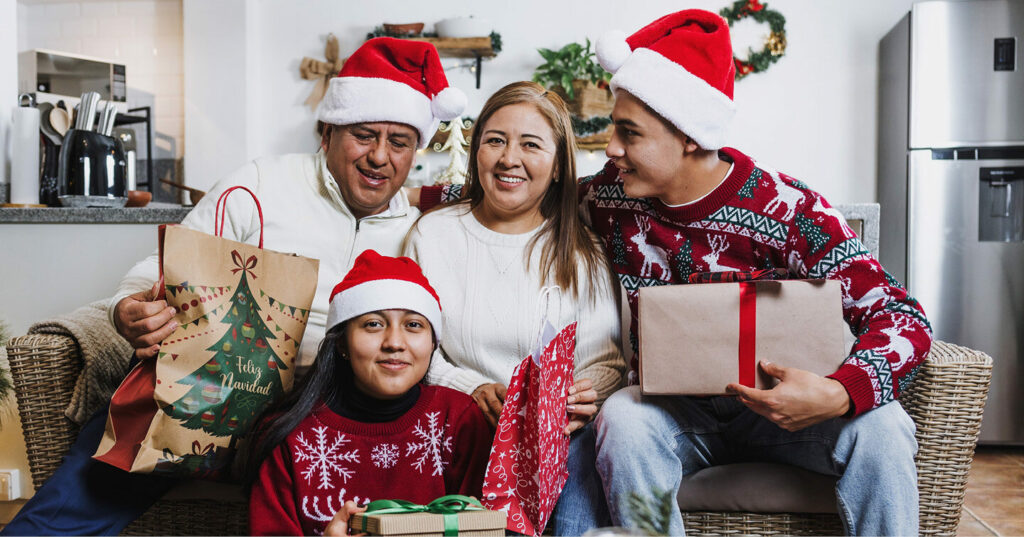 Family sitting together in a living room wearing Santa hats and holding wrapped Christmas gifts