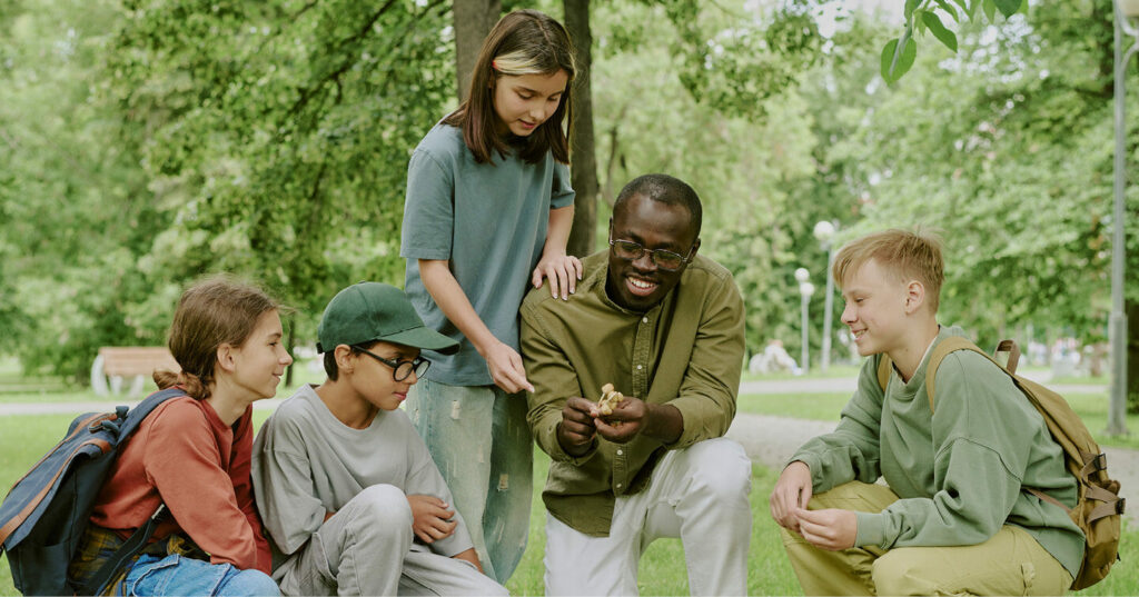 Instructor showing an object to students gathered in a park during an outdoor lesson.