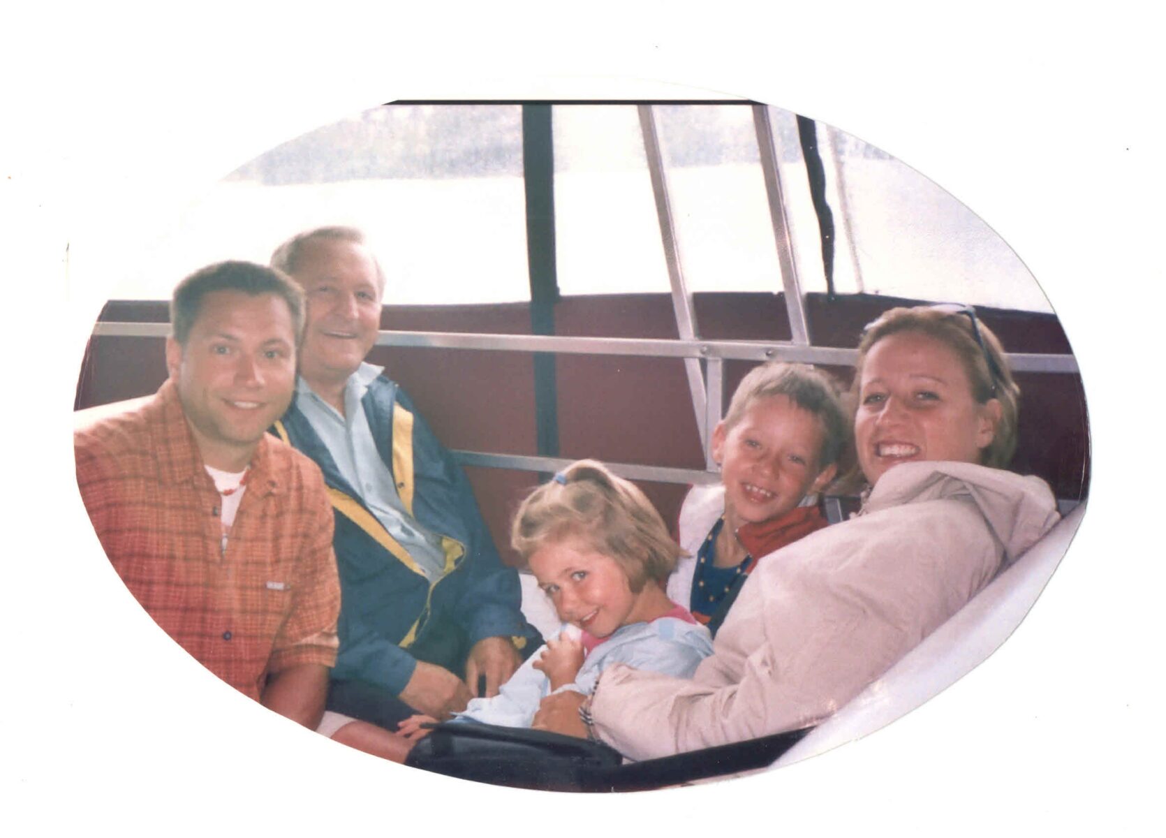 Group of people sitting in a boat cabin during a daytime ride with water visible through the windows.