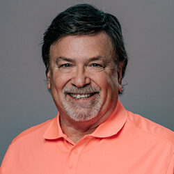 Person wearing a coral-colored polo shirt posed against a plain gray studio background.