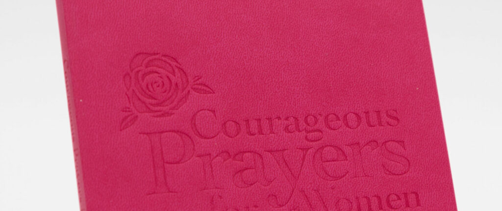 A close-up of a textured pink faux‑leather book cover featuring an embossed floral design and embossed lettering.