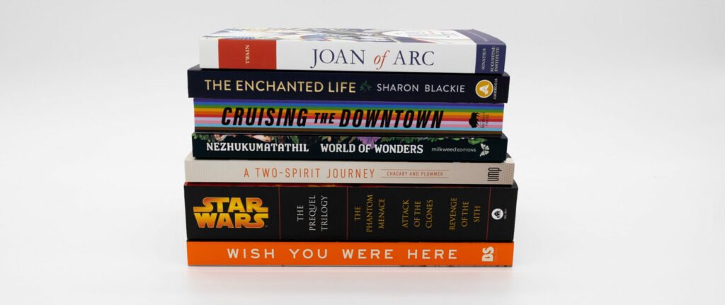 A neatly stacked pile of soft cover books of various colors and thicknesses arranged on a white surface.