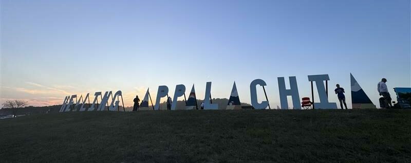 Large “Meeting Appalachia” outdoor sign with people standing around it at sunset.