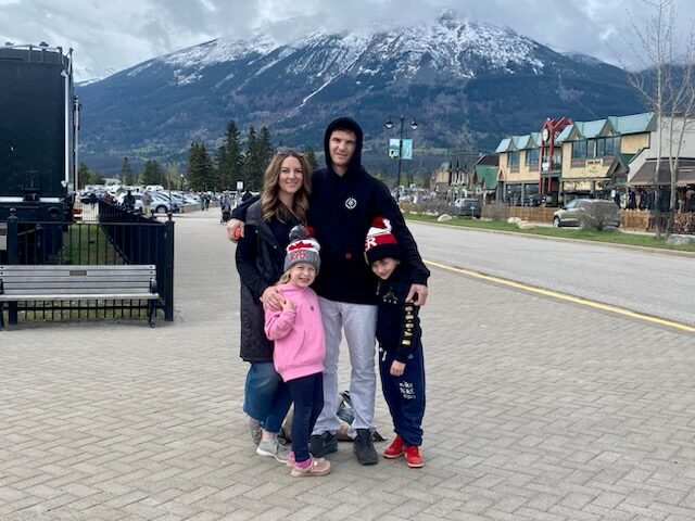 Family standing together in Jasper townsite with snow‑topped mountains and shops in the background.