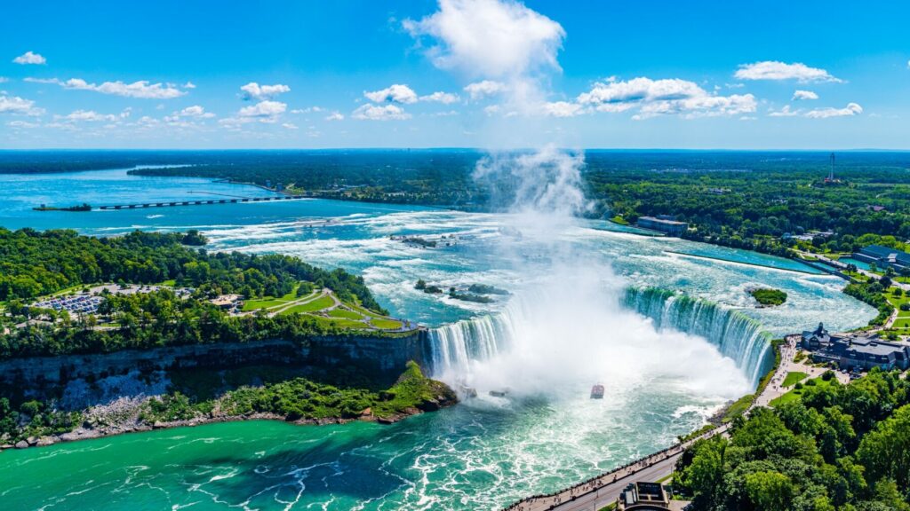 Aerial view of Niagara Falls with mist rising and turquoise water flowing through the gorge on a clear day.