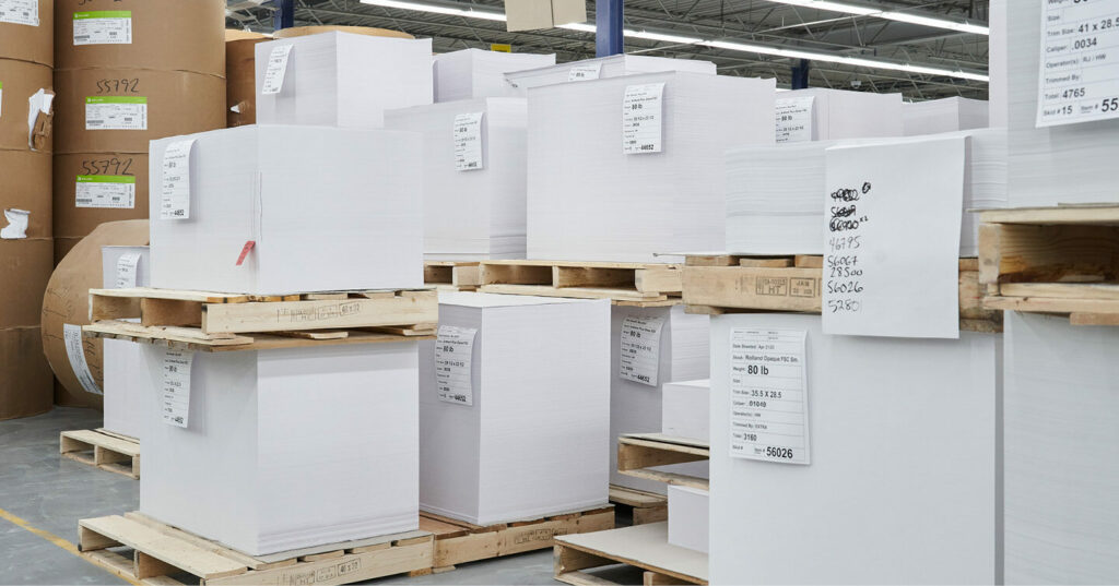 Large stacks of cut printing paper organized on wooden pallets.