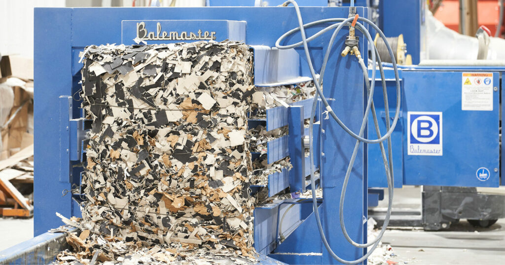 A dense bale of shredded paper being compressed inside a blue industrial baler.