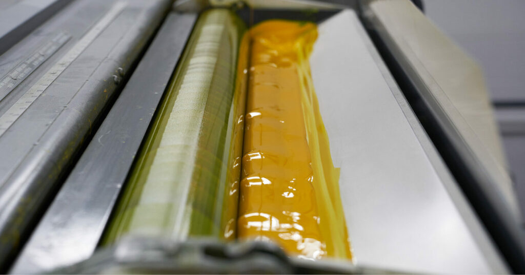 Close‑up of a printing press roller coated with bright yellow offset ink.