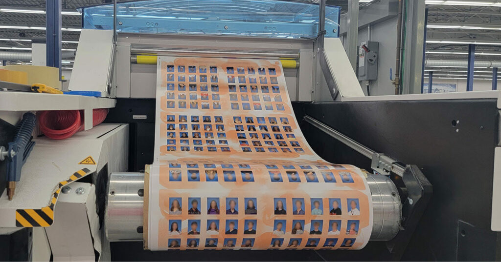 A production machine printing a continuous roll of yearbook portrait pages, showing multiple rows of student photos on an orange background.