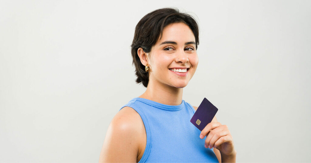 A person in a blue sleeveless top holding a credit card against a light background.