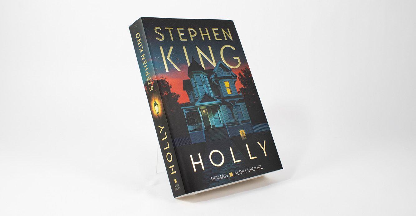 Standing copy of Stephen King’s novel Holly featuring an illustrated house at dusk on the front cover