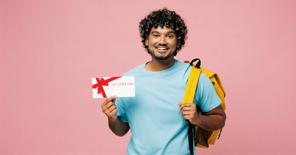 A student holding a gift voucher in one hand and wearing a backpack, standing against a pink background.