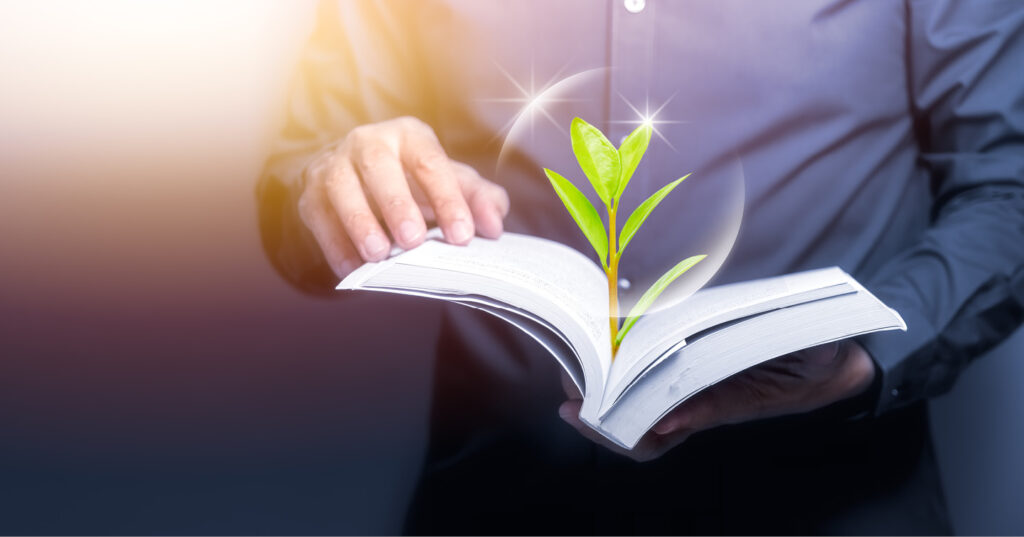 Hands opening a book with a glowing green plant sprouting from its page.