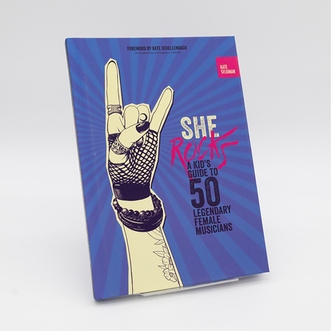 Cover of the book She Rocks: A Kid’s Guide to 50 Legendary Female Musicians, featuring an illustrated hand making a rock‑and‑roll gesture against a blue radiating background.
