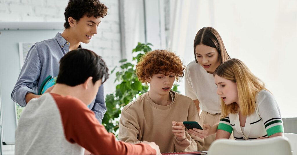 A small group of students gathered around a table, looking at a phone and discussing something together.